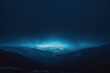 © KirKam - Mysterious Blue Glow Illuminating Snow-Covered Peaks in a Dark Mountainous Landscape.