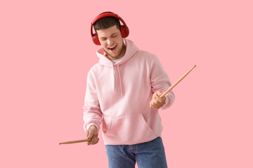 Sticker - Young bearded man in headphones with drumsticks on pink background