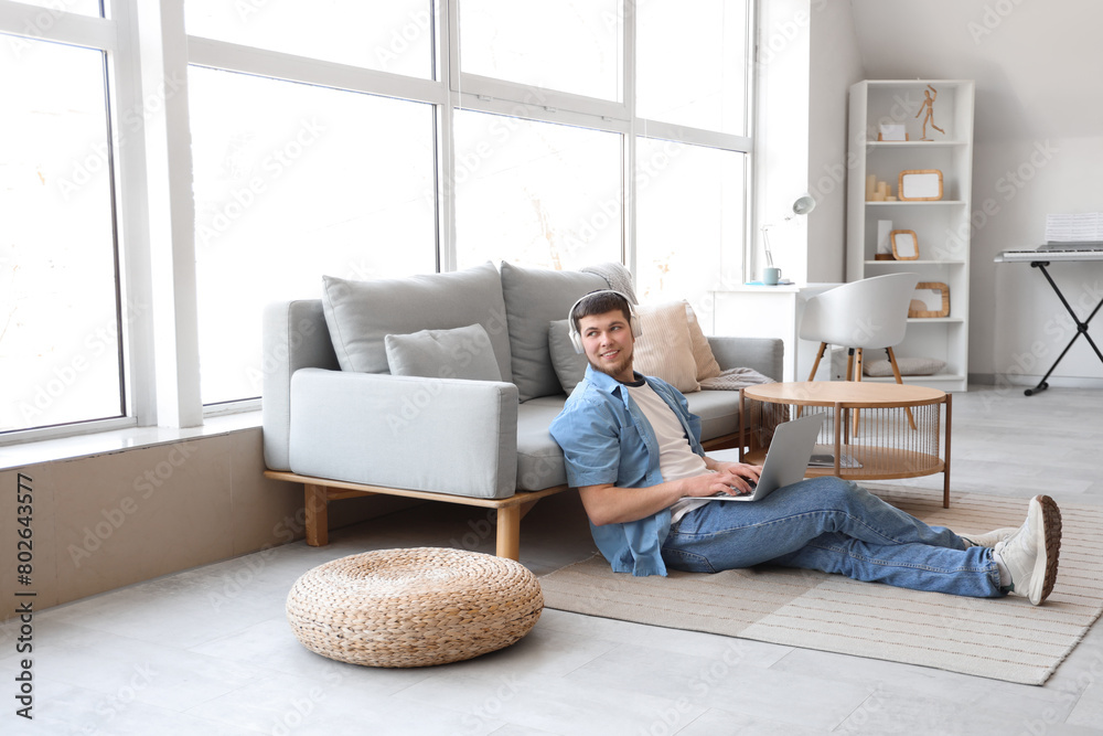 Young bearded man in headphones using laptop on floor at home