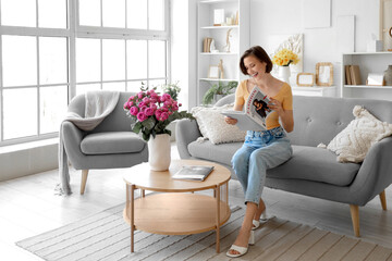 Canvas Print - Young woman with pink roses in vase reading magazine at home