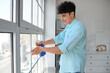 © Pixel-Shot - Young man cleaning window with squeegee at home