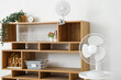 Interior of living room with modern electric fans and decor on wooden shelves