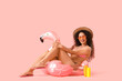 Young African-American woman with sun made of sunscreen cream and swim ring on pink background