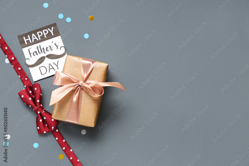 Gift box, bow-tie and greeting card with text HAPPY FATHER'S DAY on grey background. Top view