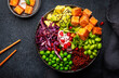 Vegan Buddha Bowl for balanced diet with roasted tofu, red quinoa, vegetables, legumes, seeds and sprouts. Black table background, top view