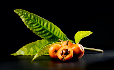 Canvas Print - Loquat fruit or Japanese medlars, Nispero, Eriobotrya japonica with leaves fresh ripe bio vegetarian food, medlar berries. Close up. On black table background