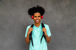 Happy teen African American boy with afro hairstyle looking at camera wearing headphones and backpack.