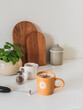A cozy morning - fresh cappuccino with cinnamon, a pot of mint, cutting boards on the kitchen table in the interior of the kitchen in a minimalist style