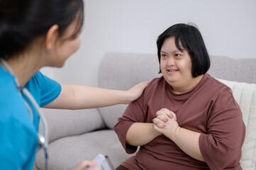 Wall Mural - Asian girl with a disability Down syndrome child fat Smiling and cute talking to an Asian female nurse or therapist about obesity in the living room at home.