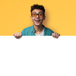 Excited man wear sunglasses glasses, braces, stand behind, peep blank empty banner mockup sign board signboard, advertise show sales slogan text, isolated against yellow background. Dental care ad