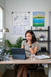 © Wasana - A woman is sitting at a desk with a laptop and a glass of water