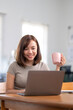 © Wasana - A woman is sitting at a table with a laptop and a pink cup