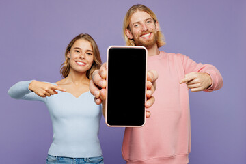 Wall Mural - Young couple two friends family man woman wearing pink blue casual clothes together hold in hand use point index finger on mobile cell phone with blank screen area isolated on plain purple background.