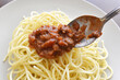 Spaghetti Bolognese with minced beef, onion, chopped tomato, garlic, olive oil, stock cube, tomato puree and Italian herb. Traditional Italian food on a white plate. Putting Bolognese on spaghetti. 