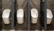Row of modern white urinals in public restroom.