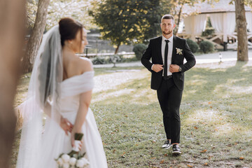 Wall Mural - A bride and groom are standing in a grassy field, with the bride holding a bouquet. The scene is intimate and romantic, with the couple looking into each other's eyes