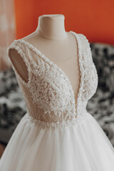 A white dress with a lace collar and a bead trim. The dress is on a mannequin and is displayed in a room with a red wall