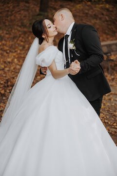 A bride and groom are kissing each other's lips. The bride is wearing a white dress and the groom is wearing a black suit