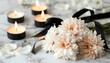 Chrysanthemum flowers with black funeral ribbon and burning candles on light background, closeup