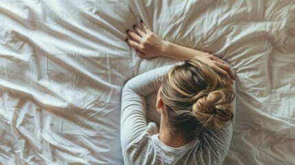 Wall Mural - A sad, crying woman lies with her back to the camera on a white bed. Depression, Stress, Nerves, Problems of the concept.