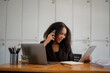 © Wasana - A woman is talking on her cell phone while sitting at a desk with two laptops and a notebook. She is smiling and she is enjoying her conversation