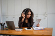 © Wasana - A woman wearing headphones and a black suit is sitting at a desk with a tablet in front of her. She is frustrated or angry, possibly due to a work-related issue