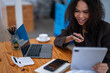 © Wasana - A woman is sitting at a desk with a laptop and tablet in front of her. She is smiling and she is enjoying her work