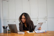 © Wasana - A woman wearing headphones is sitting at a desk with two laptops and a tablet. She is working on a project or studying