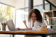 © Wasana - A woman is sitting at a desk with a laptop and smiling. She is happy and seems to be enjoying her work