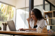 © Wasana - A woman is sitting at a desk with a laptop and smiling. She is happy and enjoying her work