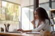 © Wasana - A woman is sitting at a desk with a laptop and smiling. She is happy and enjoying her work