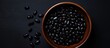 A black bowl filled with black beans is seen from above on a black background in this copy space image