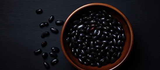 Aufkleber - A black bowl filled with black beans is seen from above on a black background in this copy space image