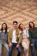 Vertical. Portrait group of cheerful friends posing together hugging looking smiling at camera. Happy generation z people leaning on brick wall outdoor. Relationships, friendship and community