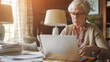 © lenblr - Senior woman working on laptop at a well-lit home office.