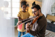 Music is so much fun. Young father teaching his little daughter to play violin and smiling.