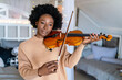 Young woman learning to play violin at home. Romantic african american girl playing violin