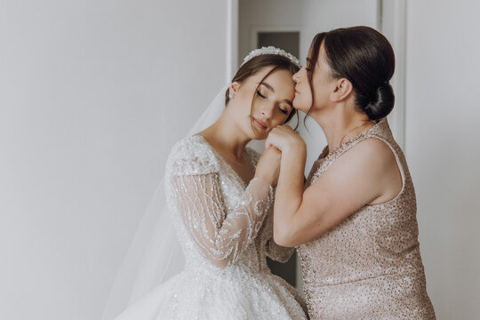 A bride is hugging her mother, who is wearing a wedding dress