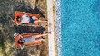 Young girls relax near swimming pool in sunbed deckchairs, women friends relax on tropical vacation in hotel resort, aerial drone view from above
