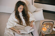 © polinaloves - Young woman reading book and drinking tea, sitting on sofa in a cozy living room.