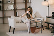 © polinaloves - Young woman reading book and drinking tea, sitting on sofa in a cozy living room.