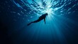 © Natalia - A silhouette of a diver swimming underwater with rays of sunlight filtering through the ocean.