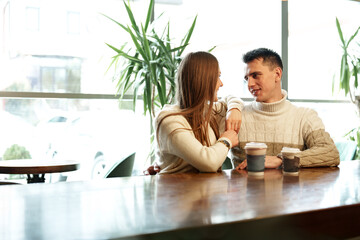 Wall Mural - Smiling Couple Enjoying Warm Beverages at a Cozy Cafe on a Sunny Afternoon