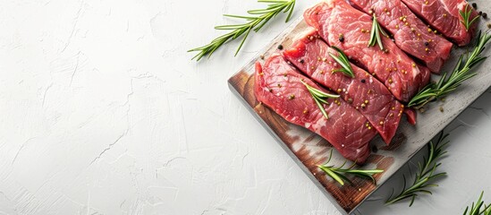 Wall Mural - Raw fresh pork pieces seasoned with rosemary on a cutting board against a light background, suitable for recipes and cooking. Top view with blank space for text.