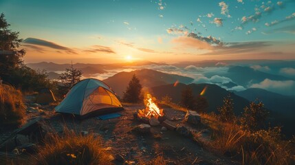 Wall Mural - A small tent is set up on a hillside with a fire burning in front of it. The sky is a beautiful orange and pink color, and the mountains in the background are covered in clouds. The scene is peaceful