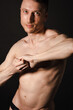 © vladorlov - A man with a beautiful body poses in the studio against a black background.
