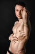 © vladorlov - A man with a beautiful body poses in the studio against a black background.