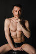 © vladorlov - A man with a beautiful body poses in the studio against a black background.