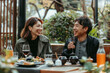 © AI_images - A Japanese couple sharing laughter during a restaurant date, sitting on the terrace. The boyfriend and girlfriend cherishing the springtime atmosphere while having lunch outdoors.