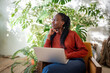 Dreaming African American woman distracted from work on laptop looks at window sits on chair, home with houseplants. Relaxed black female take break from computer rest contemplative. Procrastination.